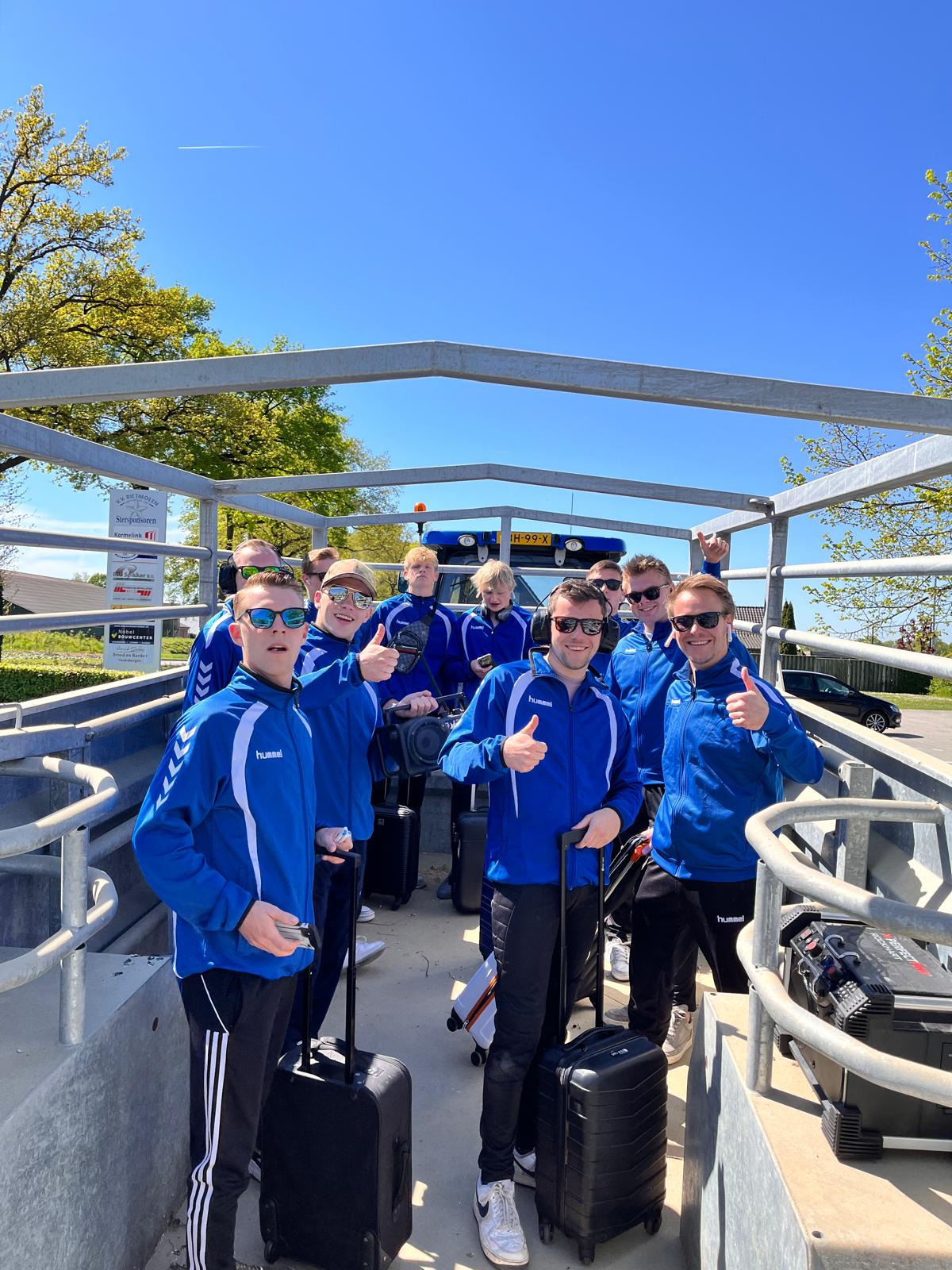 Het team in trainingspakken in de veekar, als vertrekhal geënsceneerd